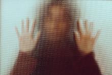 Backlit image of the silhouette of a woman with her hands pressed against a glass window.
